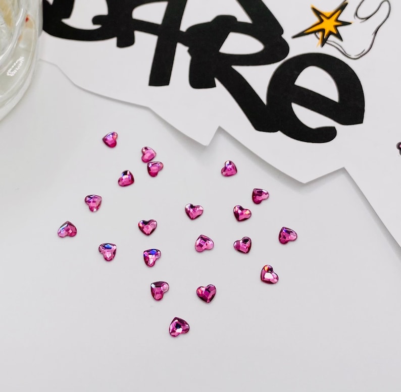 May include: A scattering of pink heart-shaped rhinestones on a white surface.