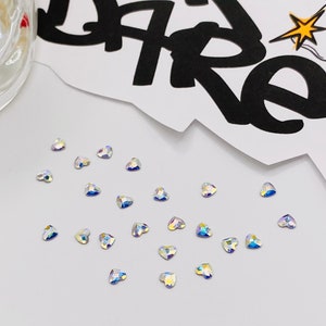 May include: A collection of iridescent heart-shaped rhinestones on a white surface.