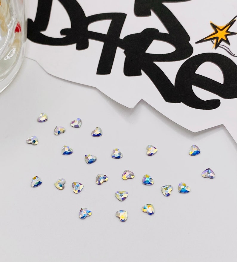 May include: A collection of iridescent heart-shaped rhinestones on a white surface.