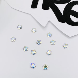 May include: A scattering of iridescent star-shaped rhinestones on a white surface.