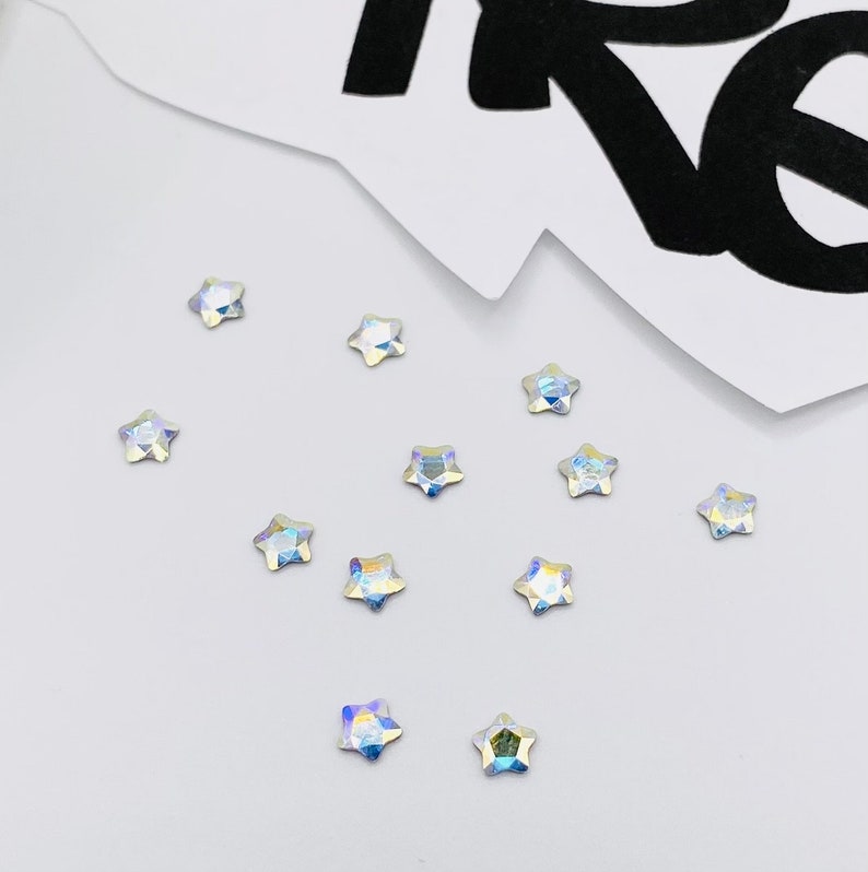 May include: A scattering of iridescent star-shaped rhinestones on a white surface.