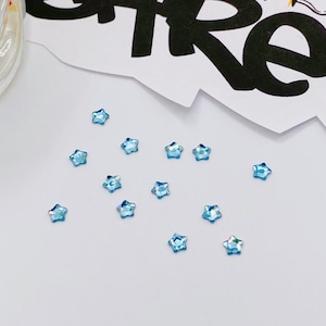 May include: A scattering of light blue star-shaped rhinestones on a white surface.