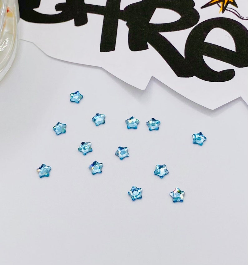 May include: A scattering of light blue star-shaped rhinestones on a white surface.