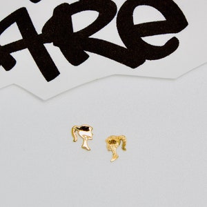 May include: A pair of gold-colored earrings shaped like a woman's profile with a ponytail.