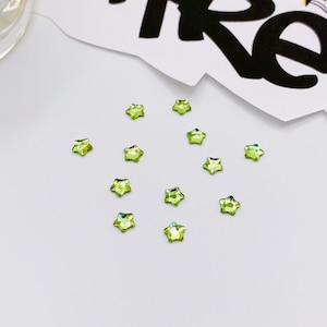 May include: A collection of 12 green star-shaped rhinestones on a white surface.