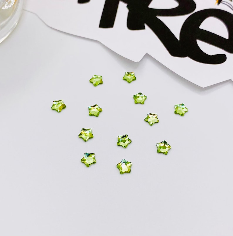 May include: A collection of 12 green star-shaped rhinestones on a white surface.