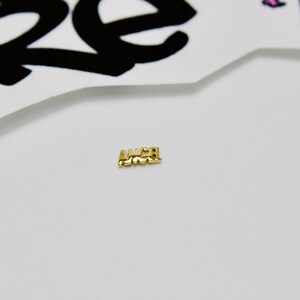 May include: A gold charm with the word "ANGEL" spelled out in all caps.