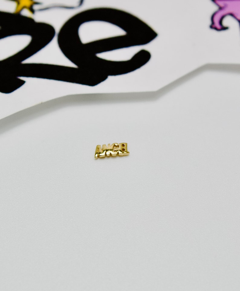 May include: A gold charm with the word "ANGEL" spelled out in all caps.