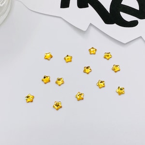 May include: A scattering of small, gold star-shaped rhinestones on a white surface.