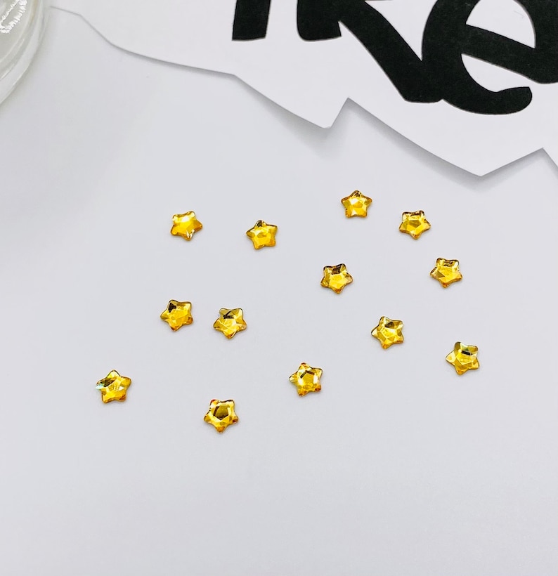 May include: A scattering of small, gold star-shaped rhinestones on a white surface.