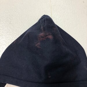 May include: A dark navy blue hooded garment featuring a pointed hood design. The fabric displays a noticeable reddish-brown discoloration or stain concentrated in the center of the hood, contrasting with the deep navy blue color of the material.