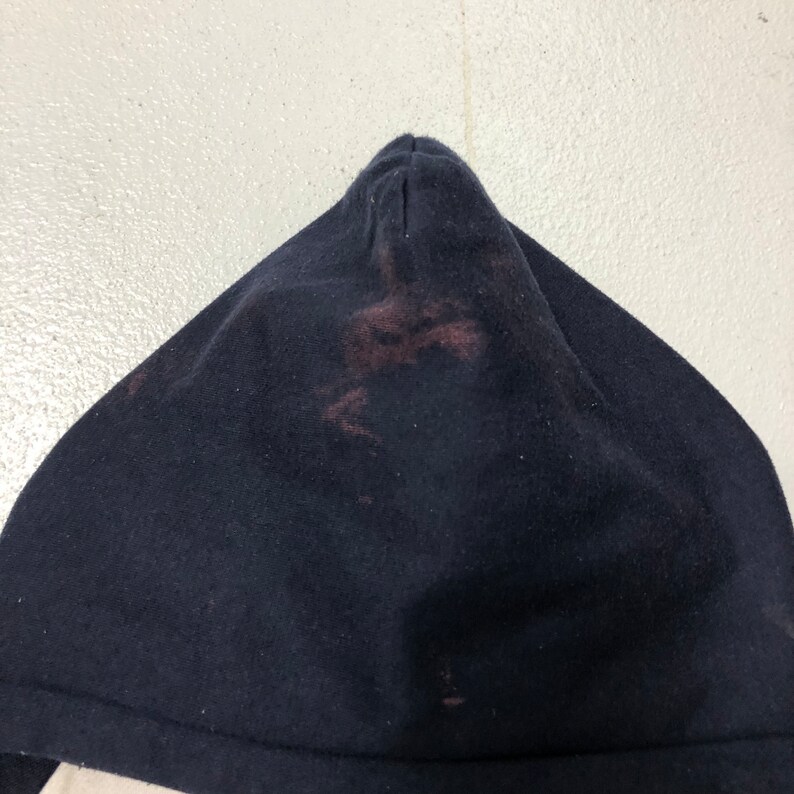 May include: A dark navy blue hooded garment featuring a pointed hood design. The fabric displays a noticeable reddish-brown discoloration or stain concentrated in the center of the hood, contrasting with the deep navy blue color of the material.