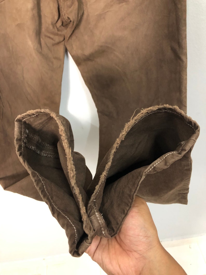 May include: Close-up of brown denim pants. The pants are a solid color with a slightly faded appearance. The cuffs are turned up, revealing the raw edge of the fabric. The pants appear to be well-worn.