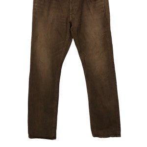 May include: Brown denim jeans with a classic five-pocket design. The pants have a straight leg cut and a button and zipper closure. The fabric has a slightly faded appearance, giving them a worn-in look.