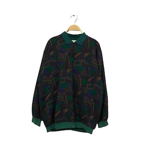 May include: A long-sleeved pullover with a geometric pattern in shades of green, purple, and brown. The collar and cuffs are solid green. The shirt is hanging on a wooden hanger against a white background.