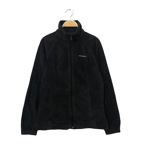 May include: Black fleece jacket with a full-length zipper and a high collar. The jacket has two front pockets and the Columbia logo on the chest. The jacket is hanging on a wooden hanger.