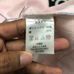 May include: A close-up of a clothing tag with Japanese text and washing instructions. The tag indicates the fabric composition is 65% polyester and 35% cotton. Additional text includes a phone number and product code.