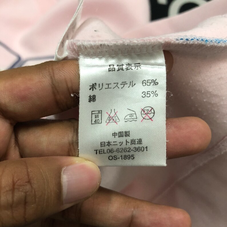 May include: A close-up of a clothing tag with Japanese text and washing instructions. The tag indicates the fabric composition is 65% polyester and 35% cotton. Additional text includes a phone number and product code.