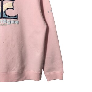 May include: Pale pink sweatshirt with embroidered text and design. The design includes the word "Courr&egrave;ges" in a stylized font, with a blue and white design above it. The sleeve has a small "c" and "u" logo.