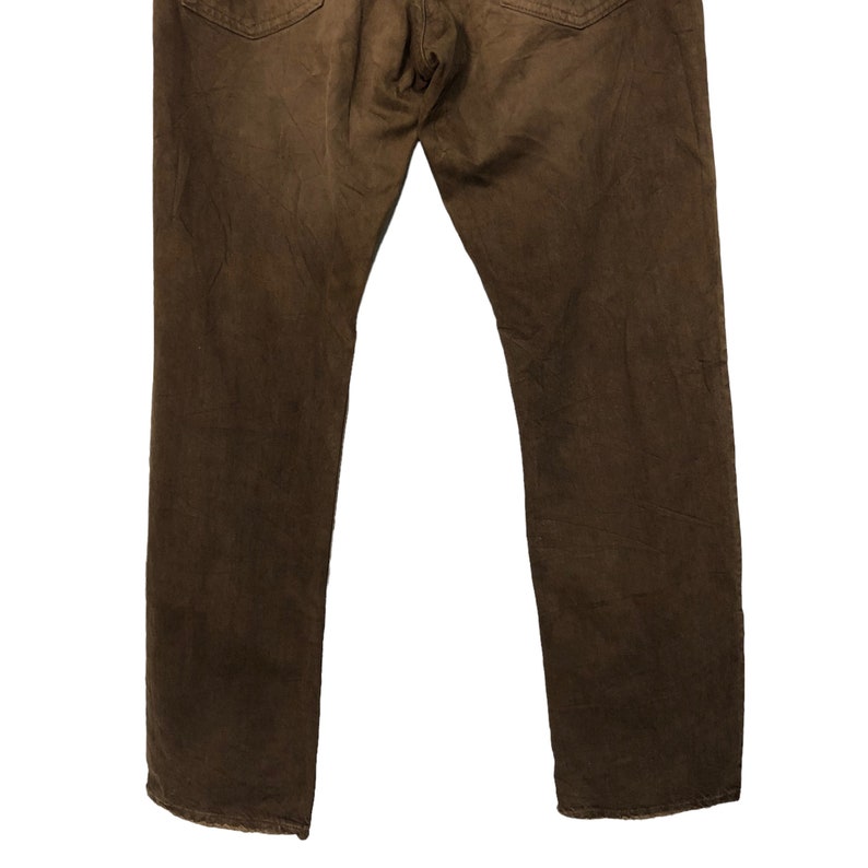 May include: A pair of brown denim jeans, viewed from the back. The jeans have a classic five-pocket design and a straight leg cut. The fabric appears to be slightly worn, giving them a vintage look. The color is a rich, earthy brown.