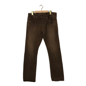 May include: Brown corduroy pants hanging on a wooden hanger. The pants have a classic five-pocket design and a button and zipper closure. The corduroy fabric has a textured appearance and a medium-brown color.