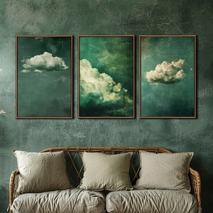 May include: Three framed cloud art prints in green and white tones hang above a rattan sofa with matching cushions. The room has a rustic, bohemian style, with a woven pendant light and a wicker chair.