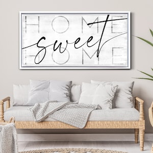 May include: A framed canvas art piece with the words "HOME sweet HOME" in black script and block letters. The background is a distressed white and gray. The frame is white.