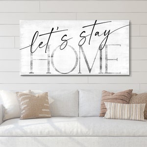 May include: White wood sign with black text that reads "Let's stay home".