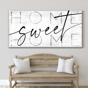 May include: A rectangular wall art piece with the words "HOME SWEET HOME" in black script and block letters on a white, textured background. Below, a wooden bench with two striped pillows.