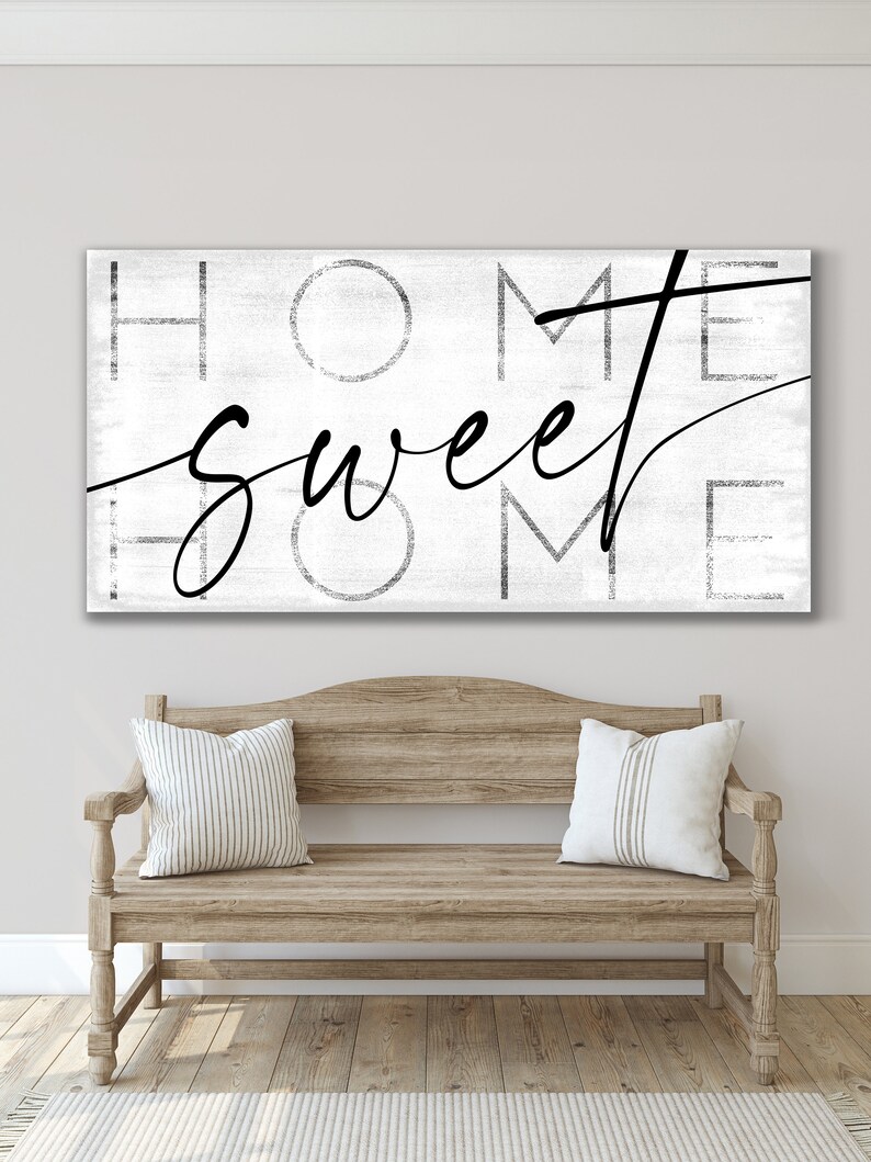 May include: A rectangular wall art piece with the words "HOME SWEET HOME" in black script and block letters on a white, textured background. Below, a wooden bench with two striped pillows.