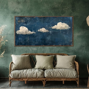 May include: A painting of three white clouds against a dark blue background, framed in a wooden frame and hanging on a green wall in a living room setting.