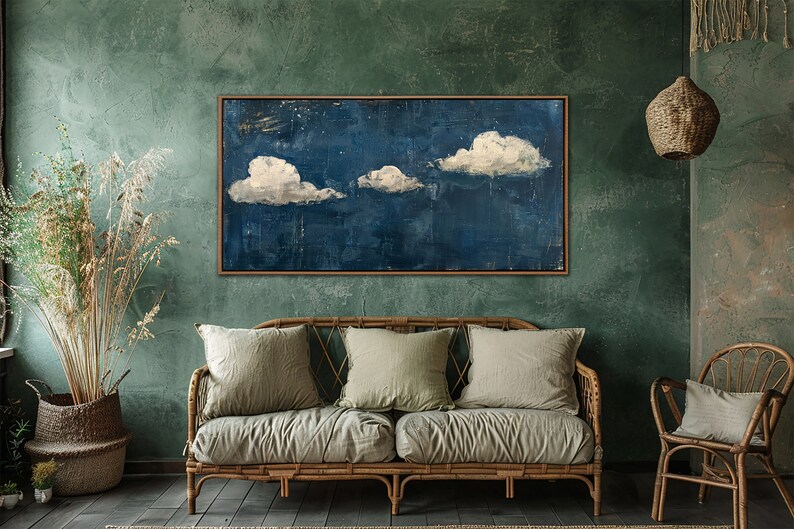 May include: A painting of three white clouds against a dark blue background, framed in a wooden frame and hanging on a green wall in a living room setting.