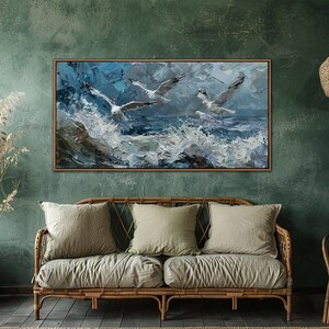 Puede incluir: Una pintura enmarcada de tres gaviotas volando sobre un mar tormentoso con olas blancas. La pintura est&aacute; en un marco de madera y est&aacute; colgada en una pared verde.