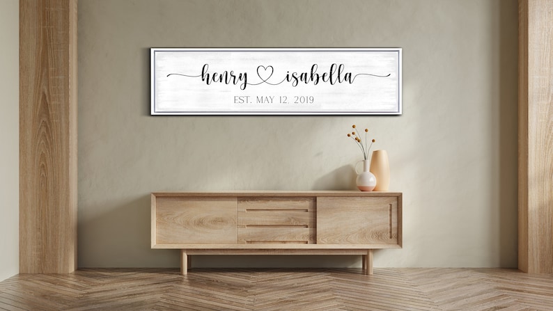 May include: A white wooden sign with black text that reads "henry & isabella est. may 12, 2019". The sign is hanging on a wall above a wooden dresser.