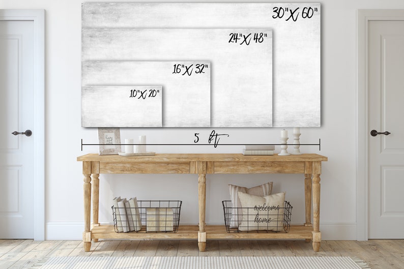 May include: A white canvas print with a wood grain texture. The print is shown in four different sizes: 10 inches by 20 inches, 16 inches by 32 inches, 24 inches by 48 inches, and 30 inches by 60 inches. The print is displayed above a wooden console table with two black wire baskets and a throw pillow with the text "welcome home".