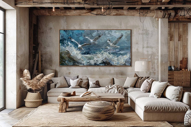 Puede incluir: Una gran pintura abstracta de tres gaviotas volando sobre un mar tormentoso. La pintura est&aacute; enmarcada en un sencillo marco de madera y cuelga de una pared de hormig&oacute;n en un sal&oacute;n. La habitaci&oacute;n cuenta con un gran sof&aacute; de esquina, una mesa de centro de madera y una alfombra tejida.