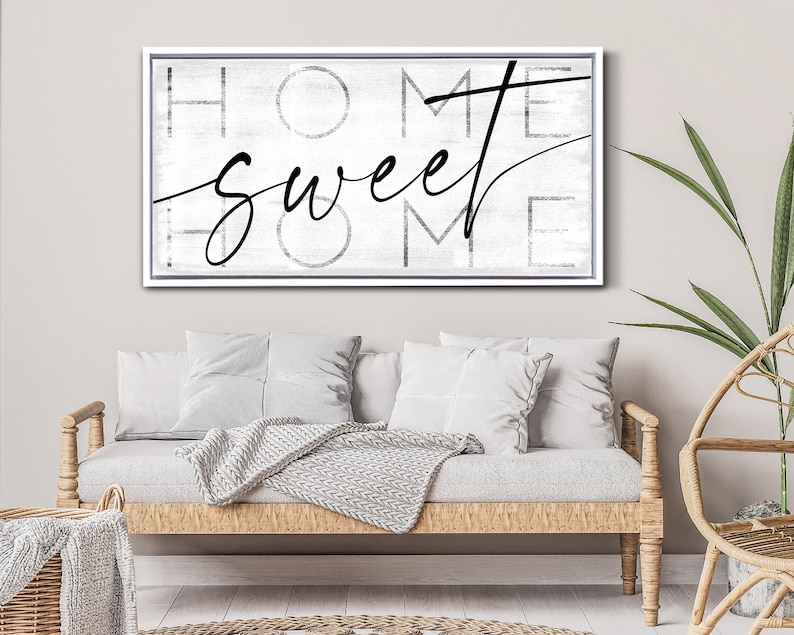 May include: A framed canvas art piece with the words "HOME sweet HOME" in black script and block letters. The background is a distressed white and gray. The frame is white.