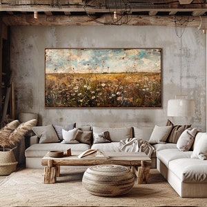 Puede incluir: Pintura de paisaje abstracto con un campo de flores silvestres bajo un cielo azul y nublado. La obra de arte est&aacute; enmarcada en madera oscura y cuelga sobre un sof&aacute; seccional beige. La habitaci&oacute;n tiene una est&eacute;tica r&uacute;stica y natural.