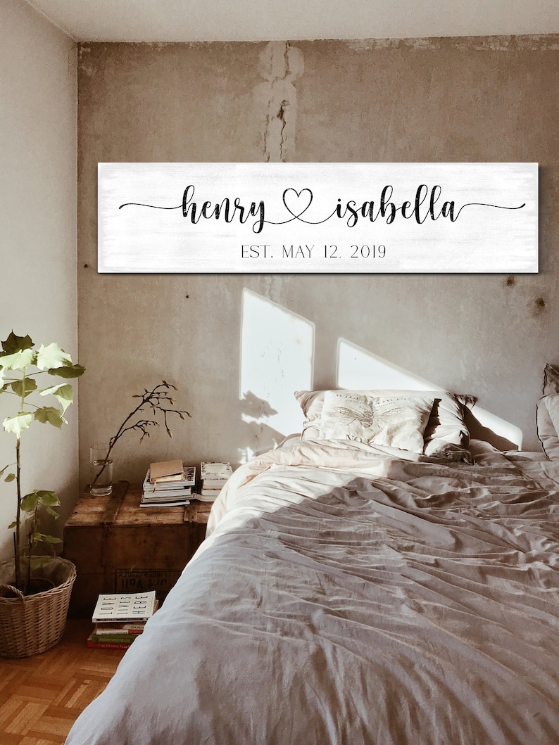 May include: White wooden sign with black calligraphy that reads "henry &hearts; isabella" and "EST. MAY 12, 2019".