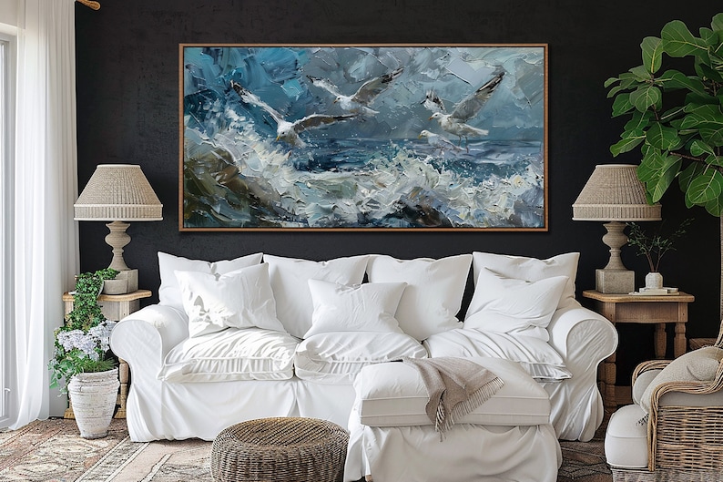 Puede incluir: Un sof&aacute; blanco con almohadas blancas y una manta en un sal&oacute;n. Un cuadro de tres gaviotas volando sobre un mar tormentoso cuelga sobre el sof&aacute;.