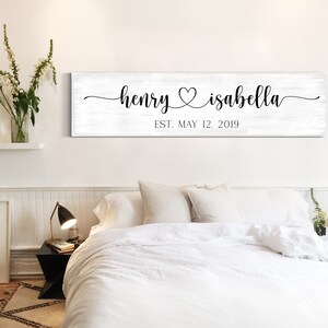 May include: White wooden sign with black calligraphy text reading "henry &hearts; isabella est. may 12, 2019".