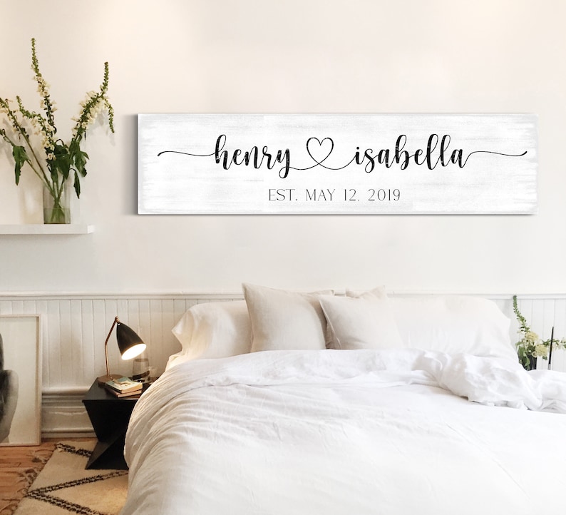 May include: White wooden sign with black calligraphy text reading "henry &hearts; isabella est. may 12, 2019".
