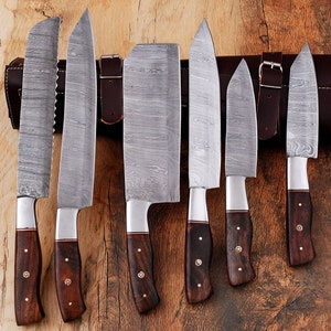 May include: Set of seven kitchen knives with wooden handles and a leather roll. The knives have a Damascus steel blade pattern.