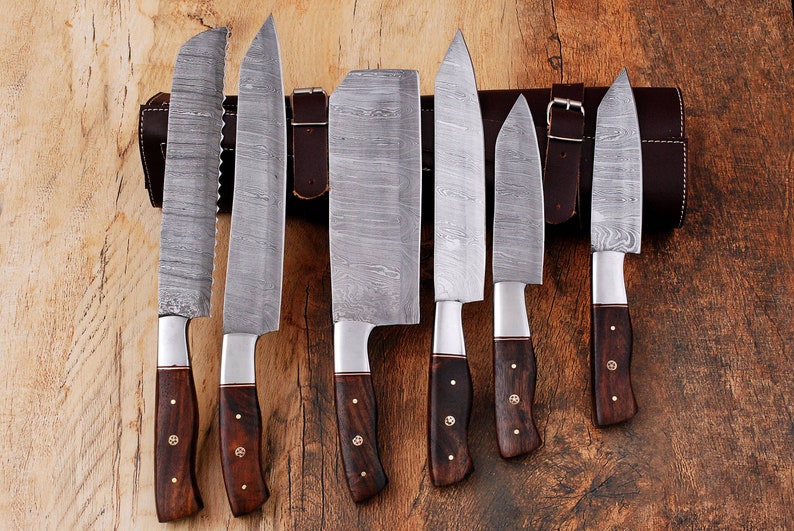 May include: Set of seven kitchen knives with wooden handles and a leather roll. The knives have a Damascus steel blade pattern.