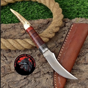 Peut inclure: Un couteau de chasse avec une lame courbe et un manche en bois de cerf brun. Le couteau est dans un fourreau en cuir brun. Le couteau porte l'inscription "Pakistan" sur la lame.