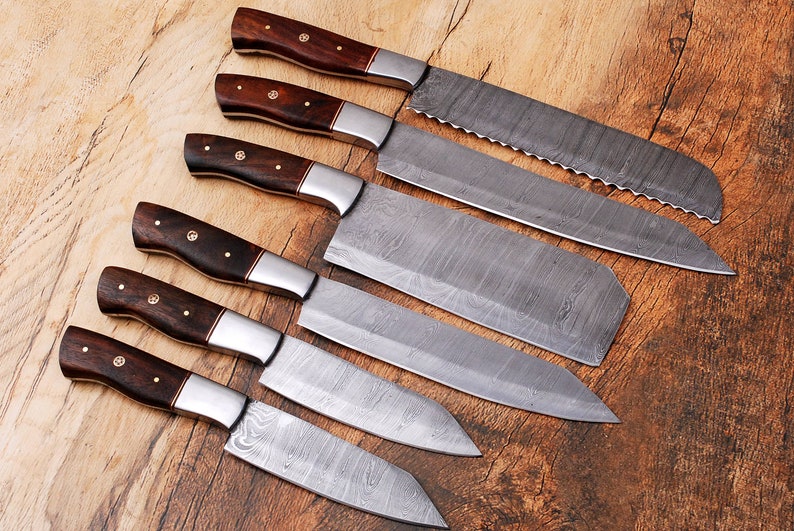 May include: Set of six kitchen knives with wooden handles. The knives have a Damascus steel blade with a wavy pattern.