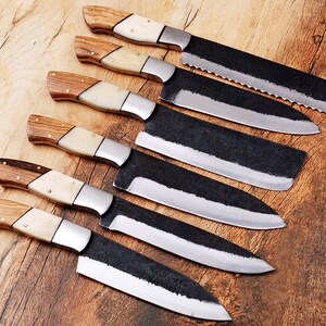 May include: A set of six kitchen knives with wooden handles and black blades. The knives are arranged in a row on a wooden surface.