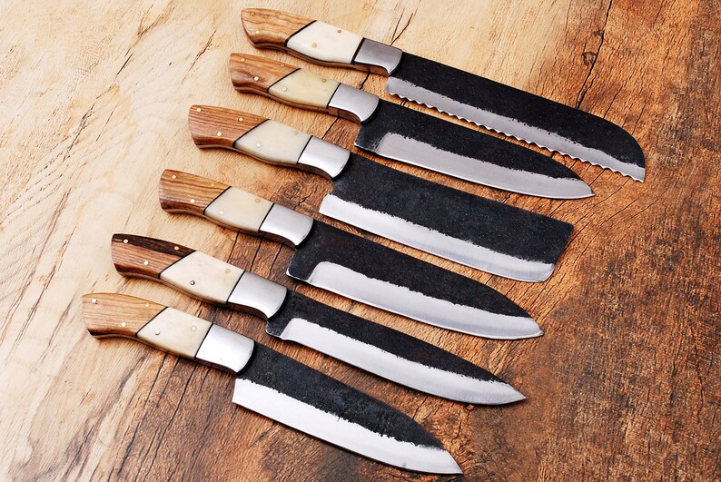 May include: A set of six kitchen knives with wooden handles and black blades. The knives are arranged in a row on a wooden surface.