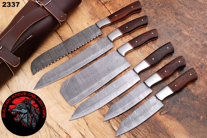 May include: Set of six Damascus steel kitchen knives with wooden handles, arranged on a wooden surface with a leather knife roll. The knives have a distinctive patterned blade and are labeled "Sultan Knife Collection".