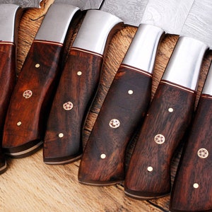May include: A set of eight kitchen knives with dark wood handles and silver blades. The handles have a decorative pattern of small gold dots and a red and gold inlay.